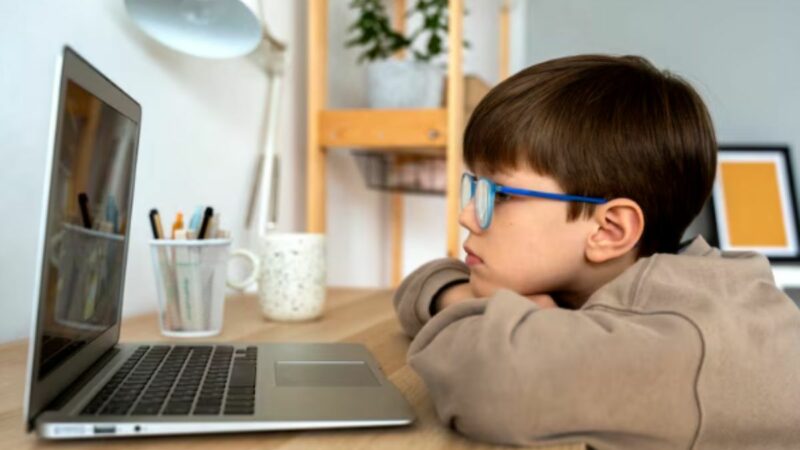 Niño con lentes frente a la pantalla de una laptop.